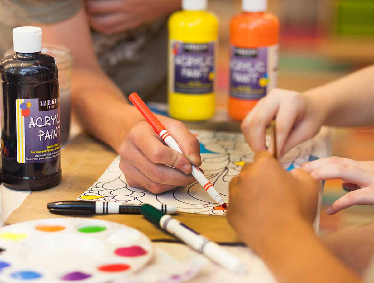 Young hands coloring with color art supplies surrounding them