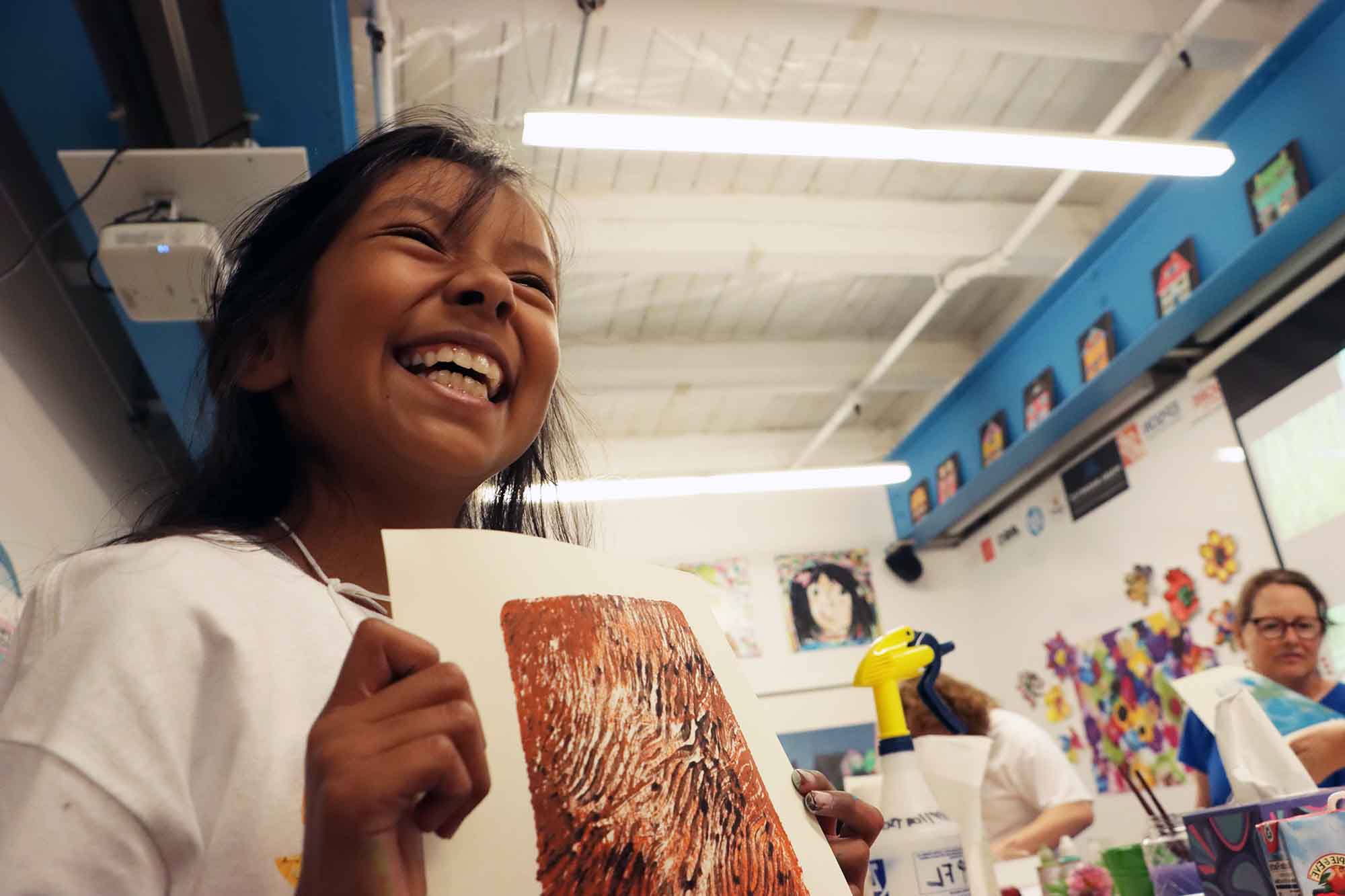 A young woman beaming with pride holding up her colorful artwork